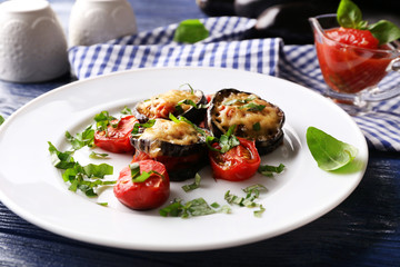 Dish of eggplant with cherry tomatoes and cheese in white plate on wooden table, closeup