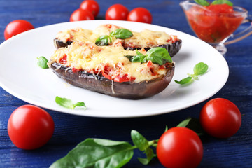 Dish of eggplant with cherry tomatoes and cheese in white plate on wooden table, closeup