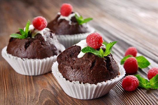 Delicious chocolate cupcakes with berries and fresh mint on wooden table close up
