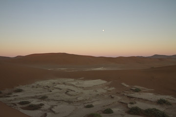 The moon sets as the sun rises over the Sossousvlei clay pan, Namib Naufluck Park, Namibia, Africa. 