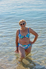 Aged lady is standing in shallow water at sea beach.