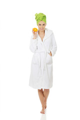 Spa woman in bathrobe holding orange.