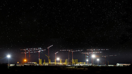 Cranes at construction site, night panorama starry sky