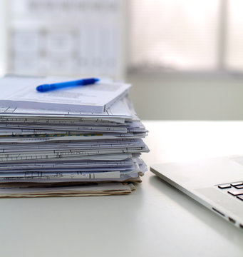 Laptop with stack of folders on table on white background