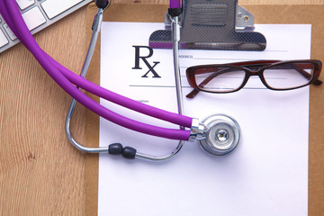 A medical stethoscope near a laptop on a wooden table, on white