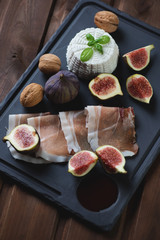 Ricotta cheese with fig fruits, ham and walnuts on a basalt dish