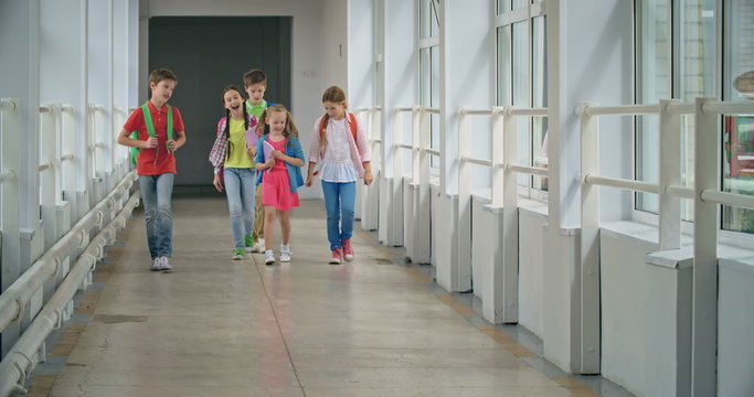 School friends approaching camera while walking along corridor and talking 