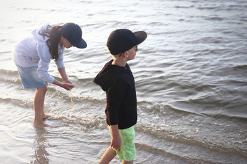 Wakacje nad morzem.
Dzieci chłopiec i dziewczynka bawią się na brzegu morza wyławiając z wody meduzy