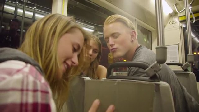 Young attractive teens watch their Ipad as they travel along on a max train