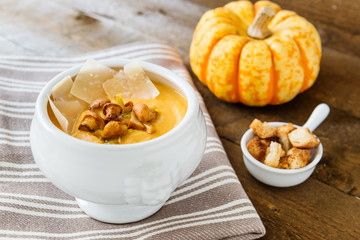 Pumpkin cream-soup with chanterelles, parmesan and croutons on the napkin. One small pumpkin for decoration