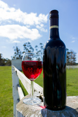 Red Wine Glass and Bottle on a White wooden Post and Rail Fence
