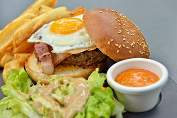 Lunch with burger, chips, eggs, sauce and salad on gray plate from stone slate