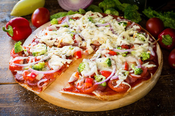 Thin crust pizza with sausages, pepper, tomatoes, broccoli and cheese on round wooden board