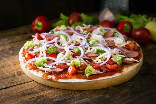 Thin crust pizza with sausages, pepper, tomatoes, broccoli and cheese on round wooden board
