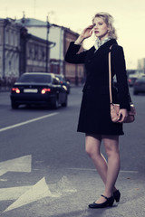 Obraz premium Fashion woman in black coat with handbag walking on the city street