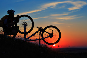 Obraz premium silhouette of man cyclist repairing a bike against sunset