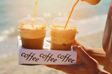 Attractive female waiters holding two ice frappe coffee on the beach near sea. Young woman enjoyng...