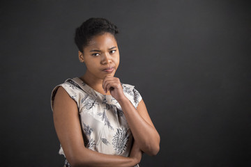 African American woman with hand on chin thinking on blackboard background
