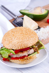 Home cooked burger with turkey, avocado, lettuce, onions, red paprika pepper on a sesame seed bun