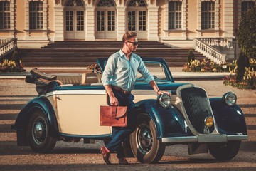 Confident wealthy young man with briefcase near classic convertible - obrazy, fototapety, plakaty