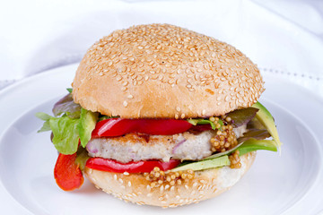 Home cooked burger with turkey, avocado, lettuce, onions, red paprika pepper on a sesame seed bun