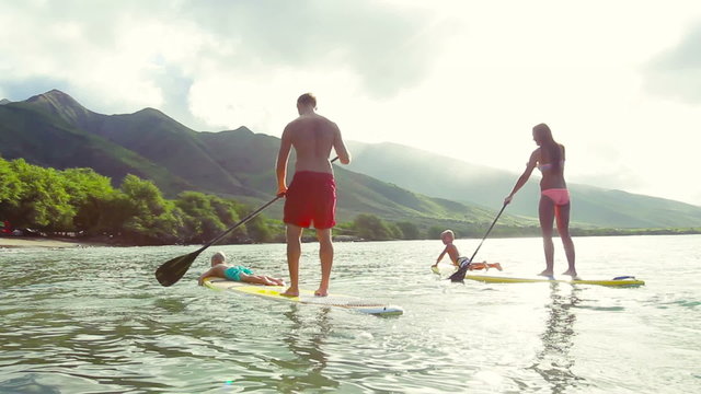 Outdoor Adventure Family Stand Up Paddle Surfing in Hawaii at Sunrise. Attractive Young Family of Four on Vacation.