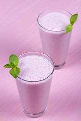 Raspberries milkshake garnished with mint on pink wooden background