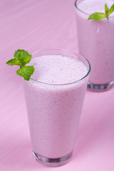 Raspberries milkshake garnished with mint on pink wooden background