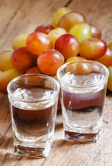 Grappa in a small glass and ripe grapes on old wooden table, sel