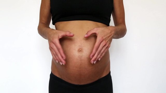 eine schwangere Frau macht ein Herz Symbol mit Ihren händen auf ihren Bauch