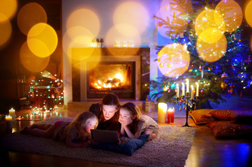 Mother and daughters using a tablet by a fireplace on Christmas