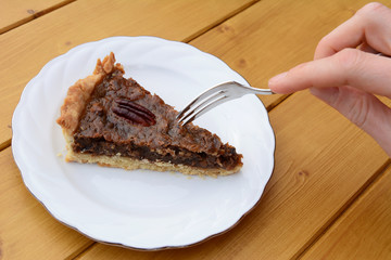 Woman uses dessert fork to cut into a slice of pecan pie