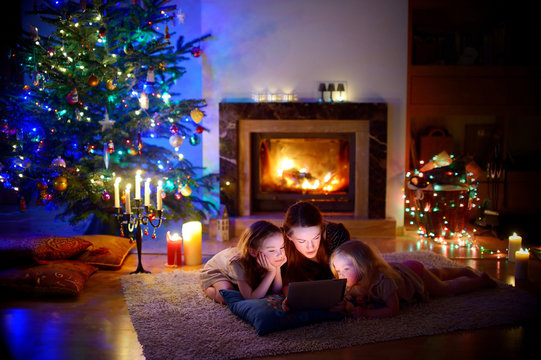 Mother and daughters using a tablet by a fireplace on Christmas