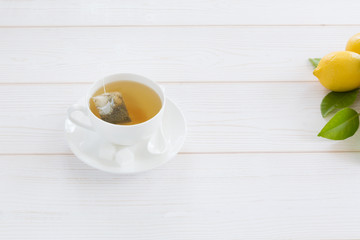 White cup with tea bag tea and lemon yellow on a white wooden background