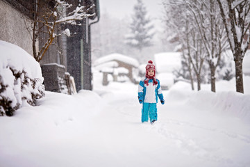 Fototapeta na wymiar little boy in a snowsuit walking through a snowy path with deep