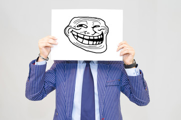 Business man hoding card with troll face on grey background - obrazy, fototapety, plakaty