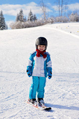 Fototapeta na wymiar Adorable little boy with blue jacket and a helmet, skiing