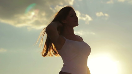 Silhouette of a young beautiful girl touching her hair in the