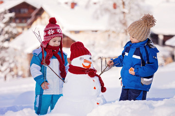 Happy beautiful children, brothers, building snowman in garden,