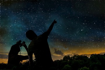 Silhouette of adult man observes night sky with child.