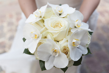 White wedding bouquet of roses and orchids in the hands of the bride