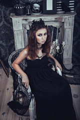 Gothic young woman in an elegant black dress in the armchair