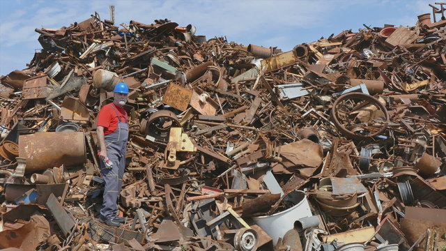 Metal recycling, worker gesturing at heap of scrap metal
