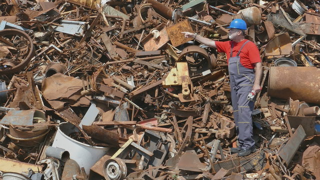 Metal recycling, worker gesturing at heap of scrap metal