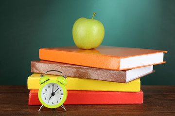 Stack of books with green apple and alarm clock on desk on green chalkboard background - Powered by Adobe