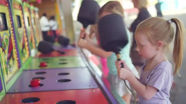 Three little girls play a carnival game and one wins a prize and shares it
