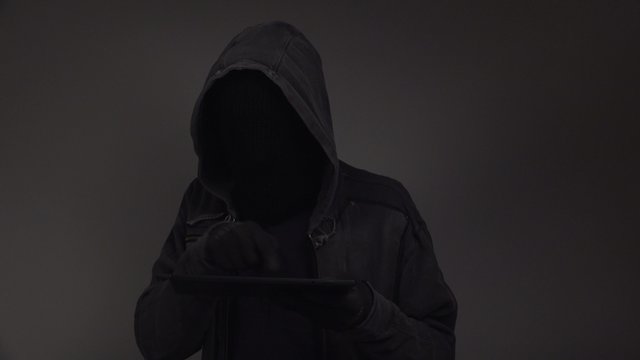 Hooded cyber criminal using digital tablet computer to access deep web internet page, p2p, piracy or network security concept, 4k uhd footage