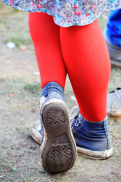 closeup on pair of worn canvas shoes with red pantyhose and skirt