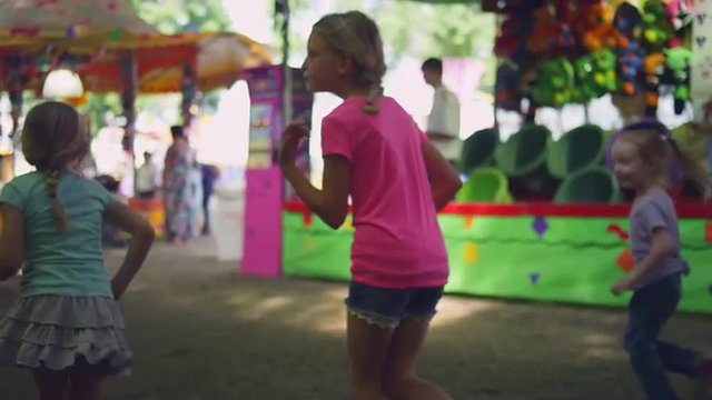 The camera follows three little girls running through a carnival, slow motion
