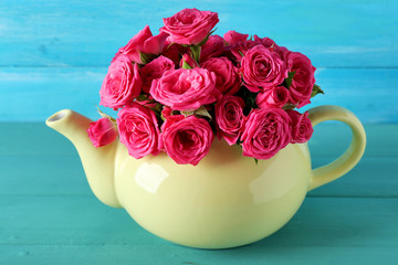Beautiful roses in teapot on wooden background